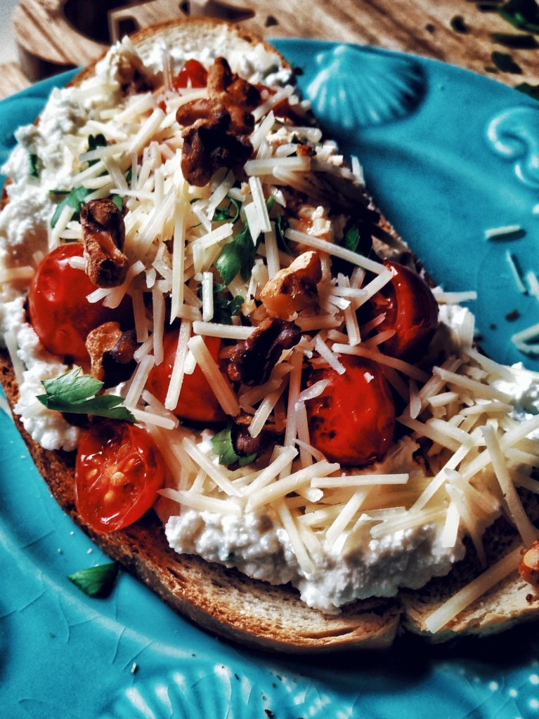 Image of Charred Tomato and Ricotta, with roasted walnuts, some minced herbs, and topped with a balsamic glaze, all resting on top of toasted sourdough bread.